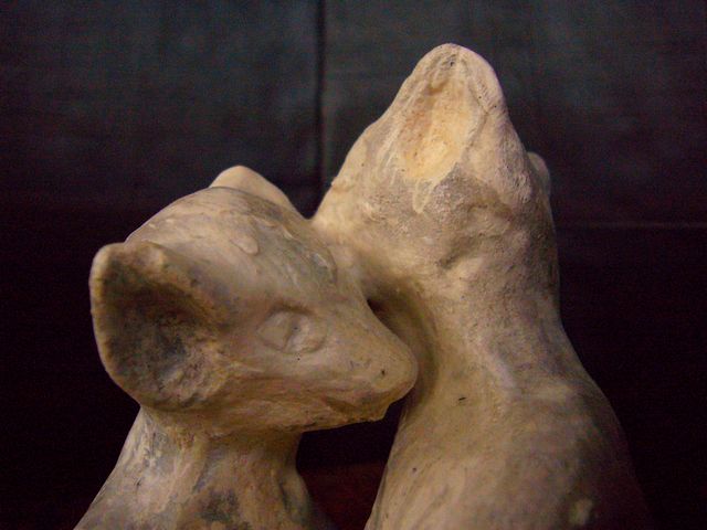 Two sculpted cat people, seated, kissing; close-up. Click to enlarge.