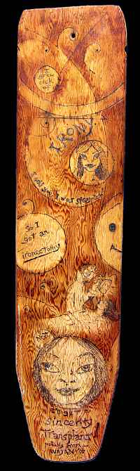 Old wooden ironing board with strong woodgrain; cartoons cut and burned into it. Black background.