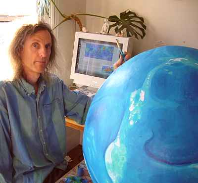 Chris Wayan sitting by Lyr, a big papier-mache planet in blue and white (the land's still unpainted).