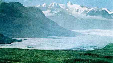 Icy peaks across a sound; low, livid green shore in foreground.