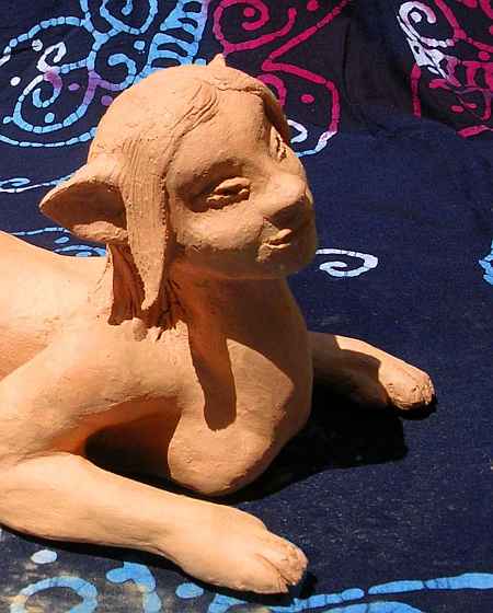 Crouching sphinx's; close-up of tilted, smiling face; unfired clay sculpture.  Click to enlarge.