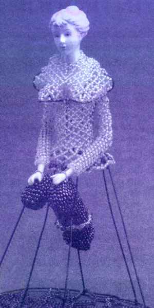 Photo of a sculpture by Joyce Scott: a figurine of a southern belle with heavily beaded blouse but an open wireframe skirt with a phallus of black beadwork thrusting in.
